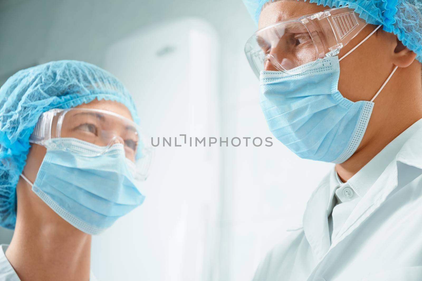 Woman and man surgeons in protective uniforms looks to each other and discuss anything