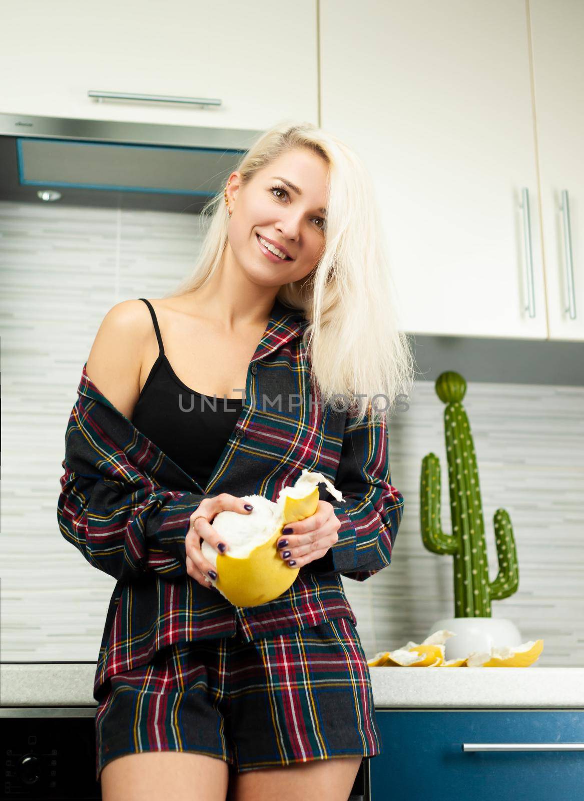 Woman in the kitchen in home clothes cleaning fruit pomelo with emotions by Rotozey