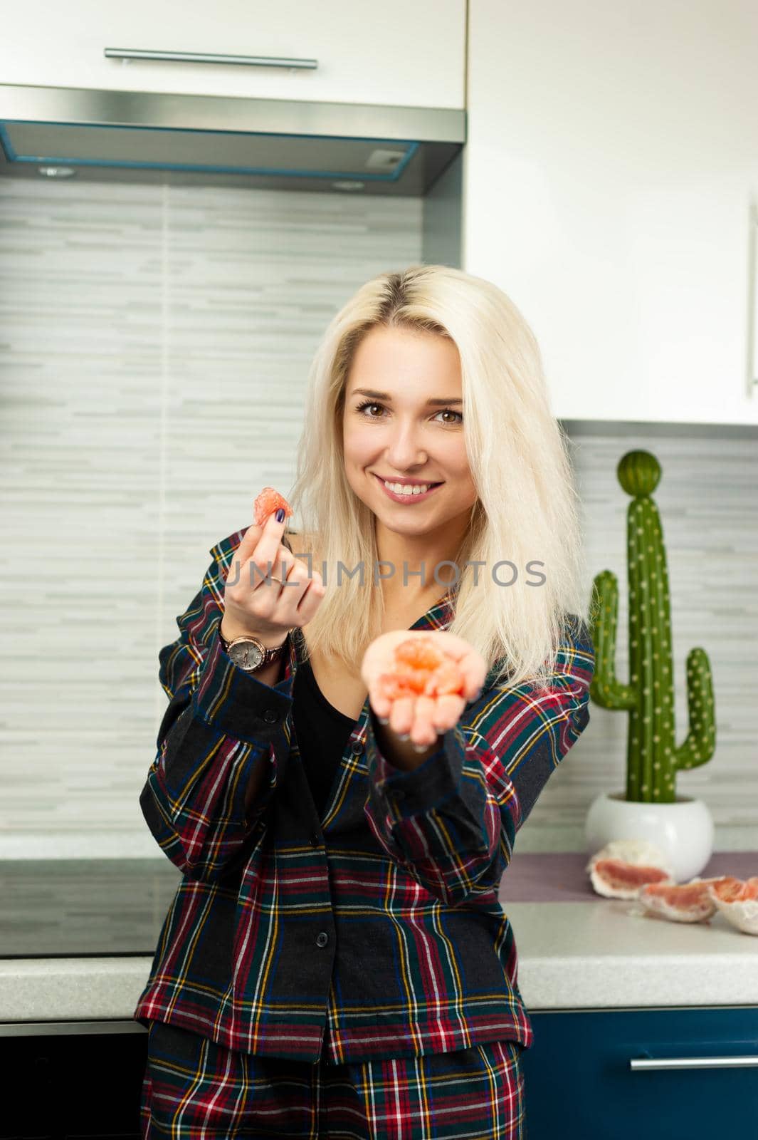 the woman in the kitchen in home clothes with a peeled pomelo fruit eats and laughs