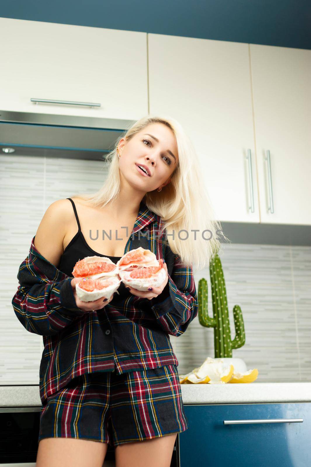 the woman in the kitchen in home clothes with a peeled pomelo fruit smiles