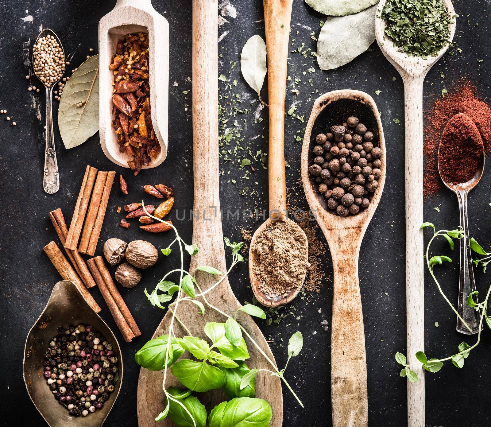 wooden spoons with spices and herbs on textured black background