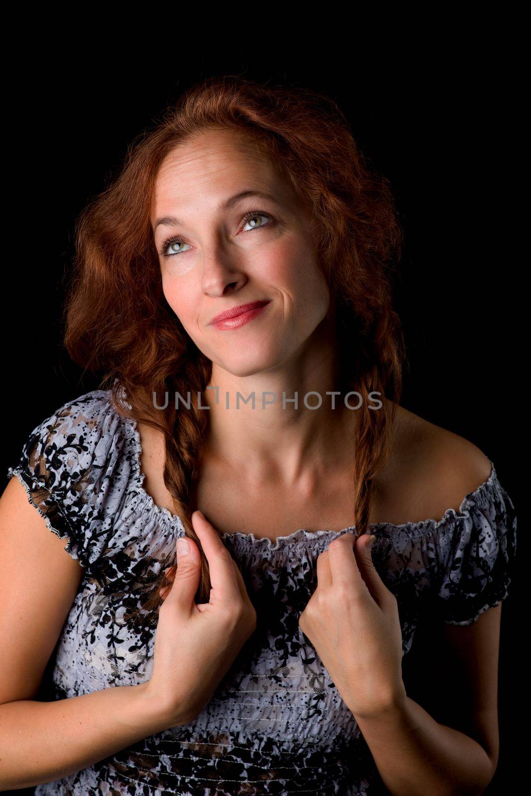 Portrait of happy woman holding two ponytails. Young woman smiling at camera against black background. Beautiful woman with brown hair wearing grey dress posing in studio