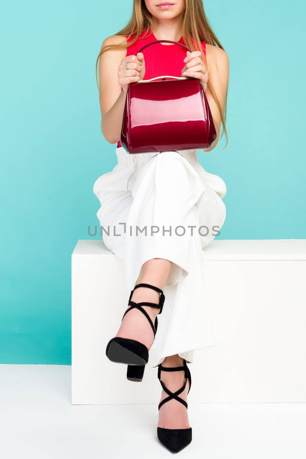 Beautiful woman sitting on the bench with red handbag purse and high heel shoes. - image