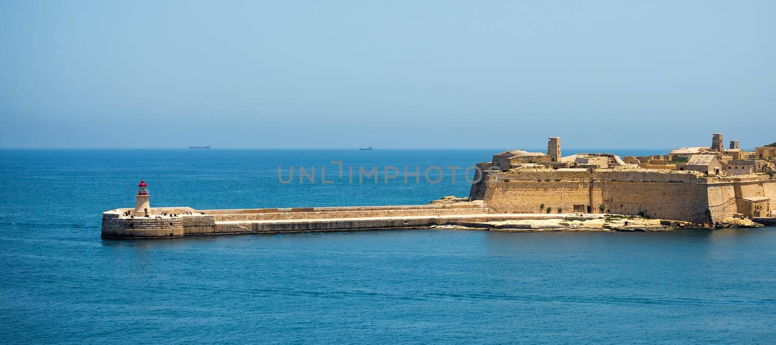 lighthouse in Valletta port of Malta on misty sea background with a ship