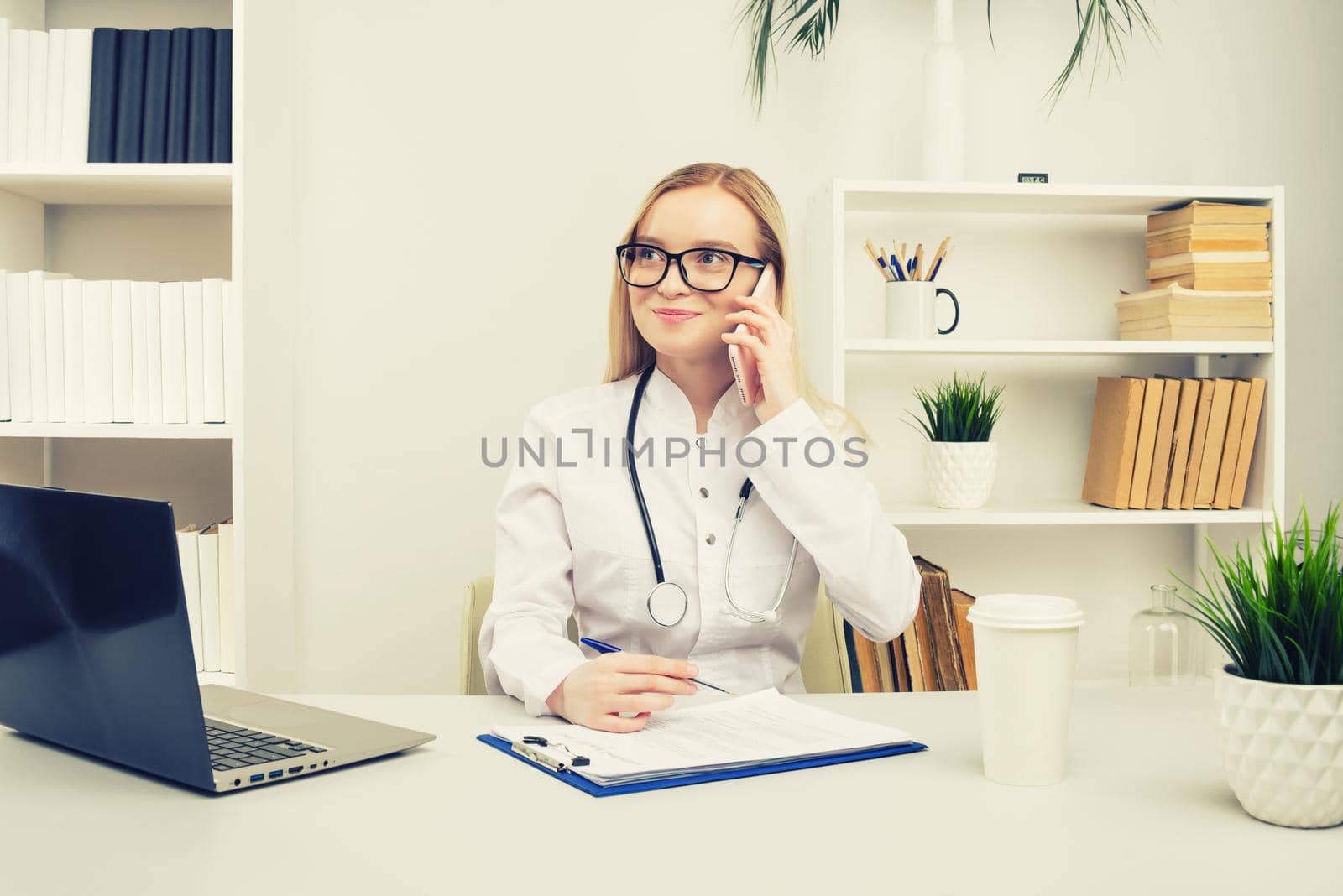 Portrait of a beautiful smiling woman doctor while talking on the smartphone and complete a medical information - Image toned