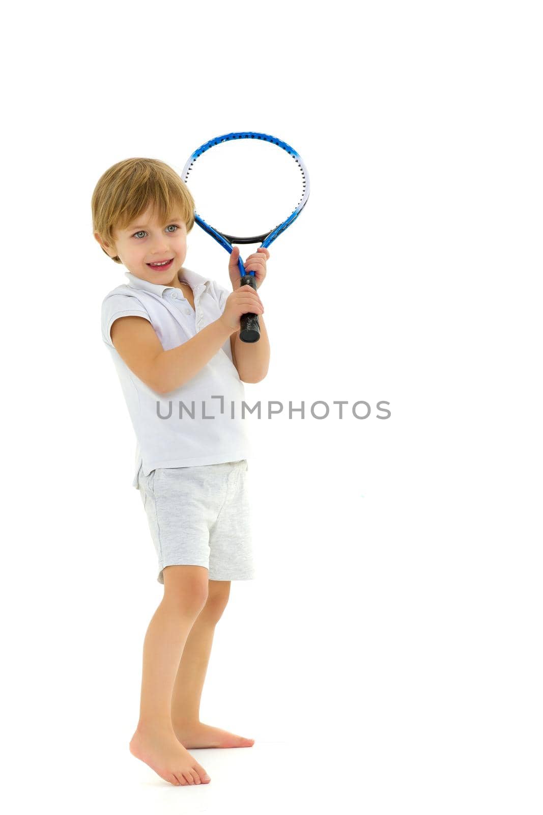 Cute little boy playing tennis. Adorable kid five years old in sports outfit holding tennis racket. Boy playing against white background. Active healthy lifestyle concept