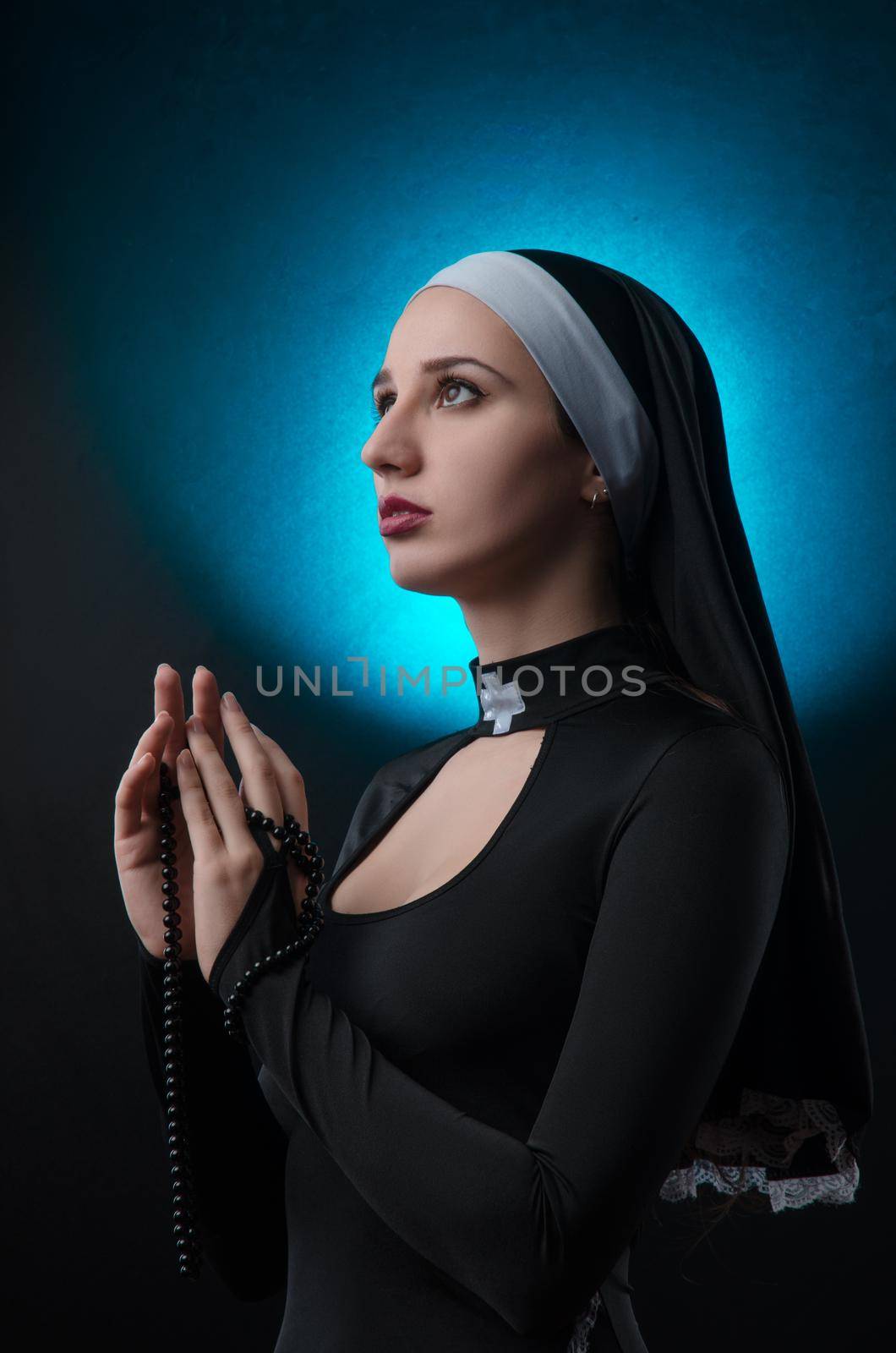 The Fine art portrait of a novice nun in deep prayer with rosary