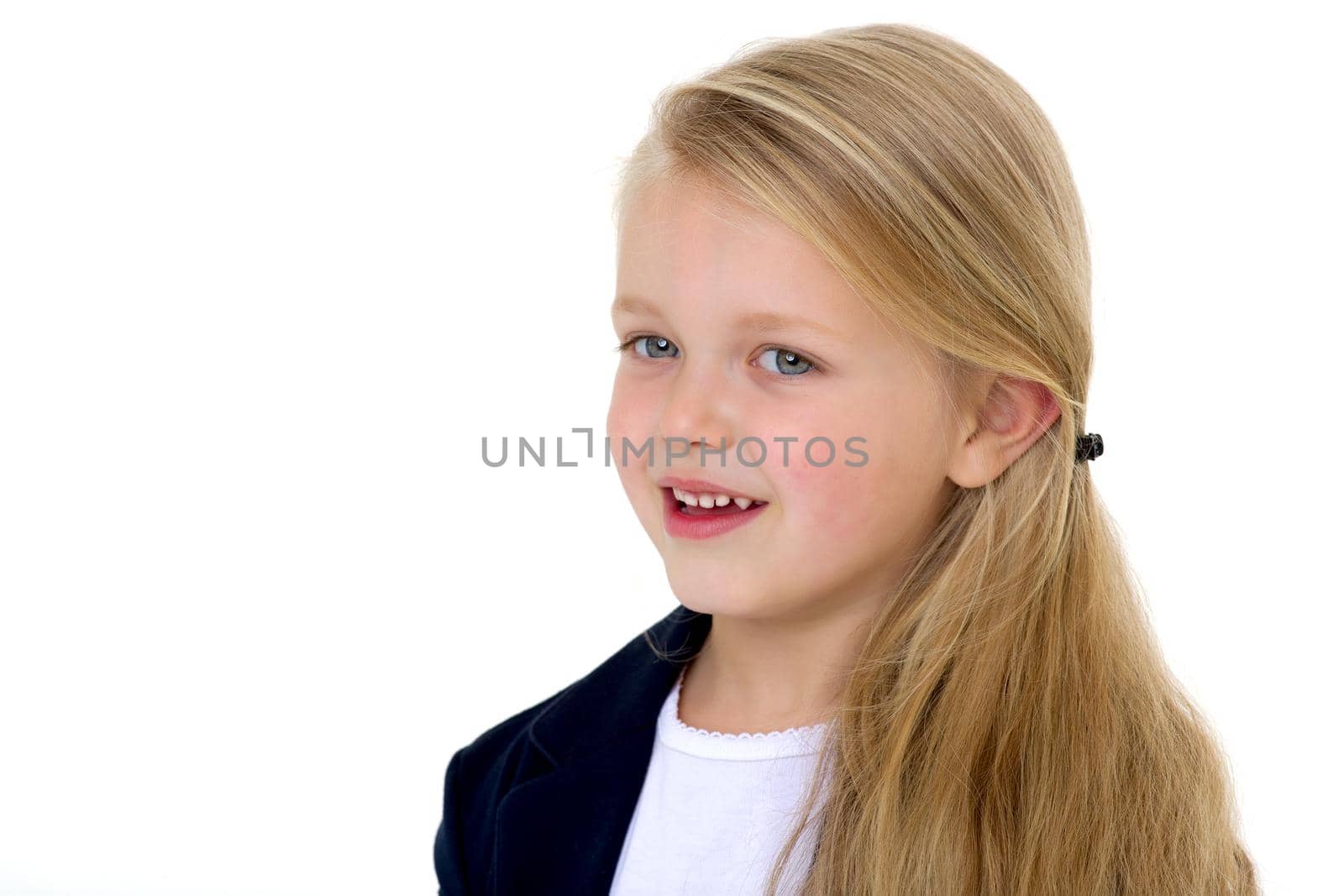 Portrait of adorable blonde little girl. Curious beautiful long haired schoolgirl standing against white background. Lovely elementary school student in blue jacket and white blouse