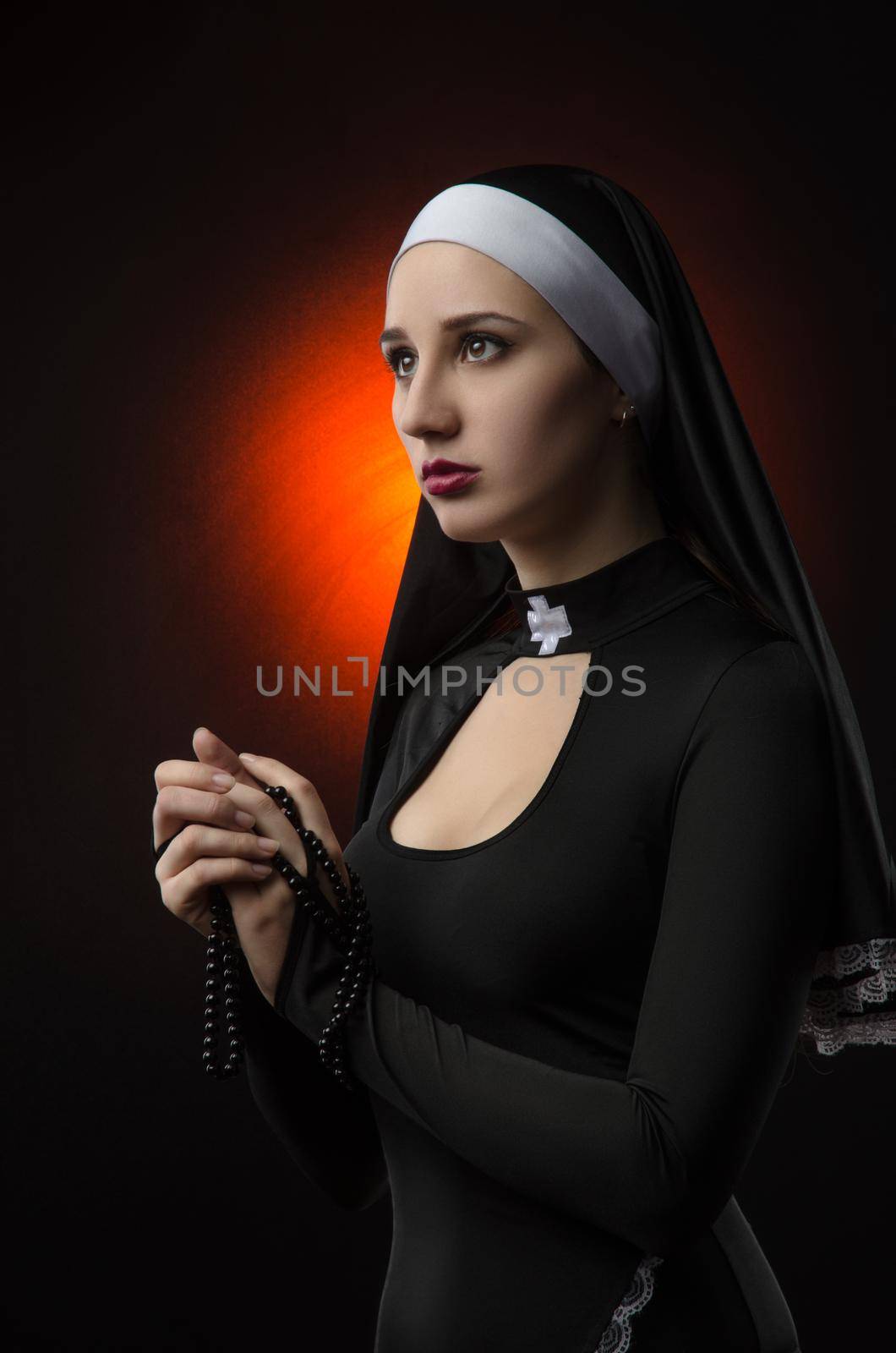 The Fine art portrait of a novice nun in deep prayer with rosary