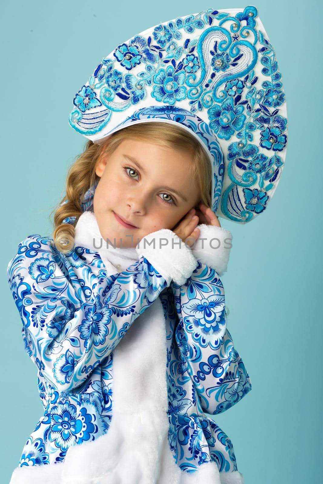 Portrait of lovely Snow Maiden girl. Happy girl dressed traditional Russian Christmas Snegurochka costume posing against light blue background. Happy Christmas and New Year concept