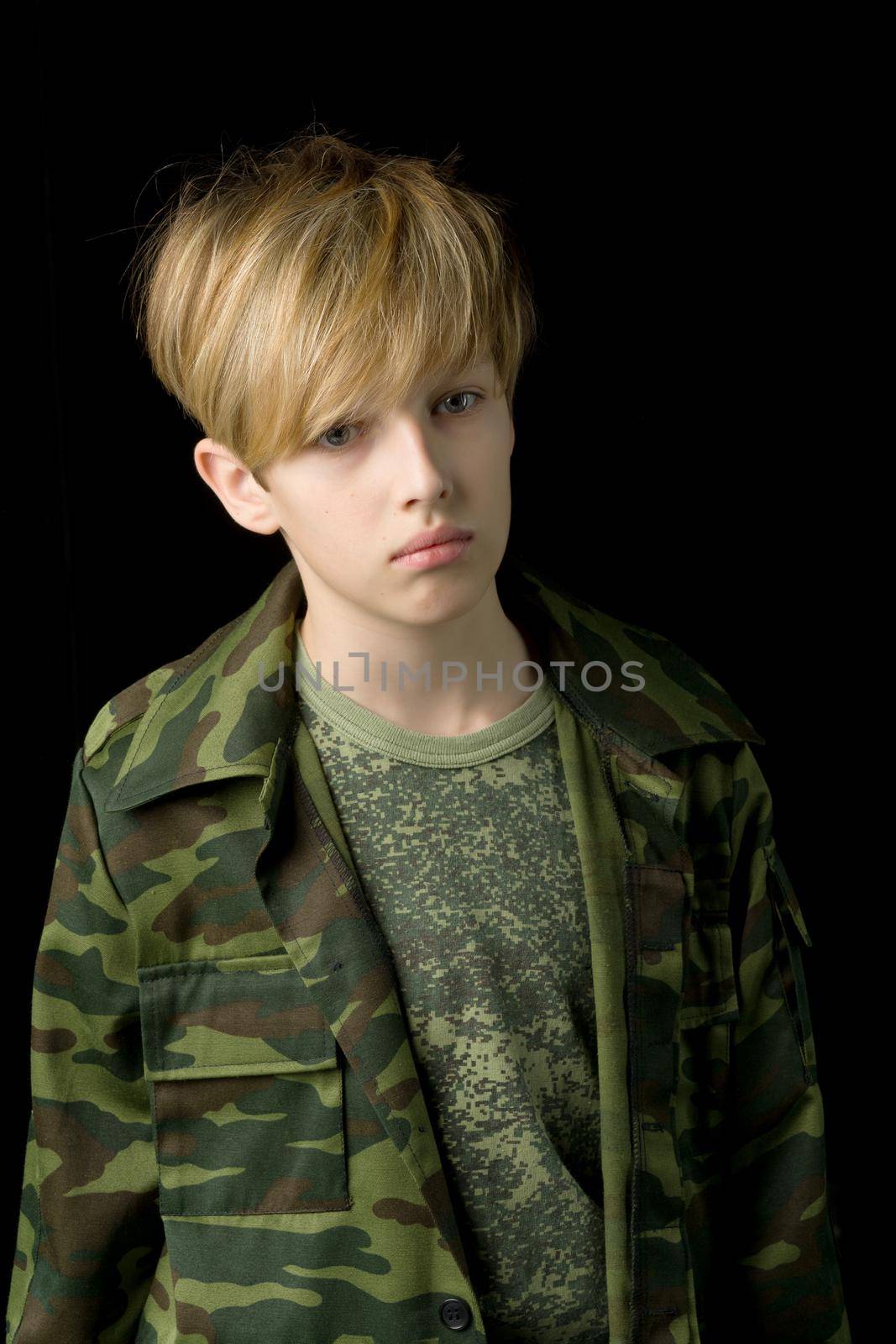 Confident teenage boy in camouflage clothing. Teenager in khaki military clothing posing on black background in studio. Boy wearing camouflage t-shirt and military jacket