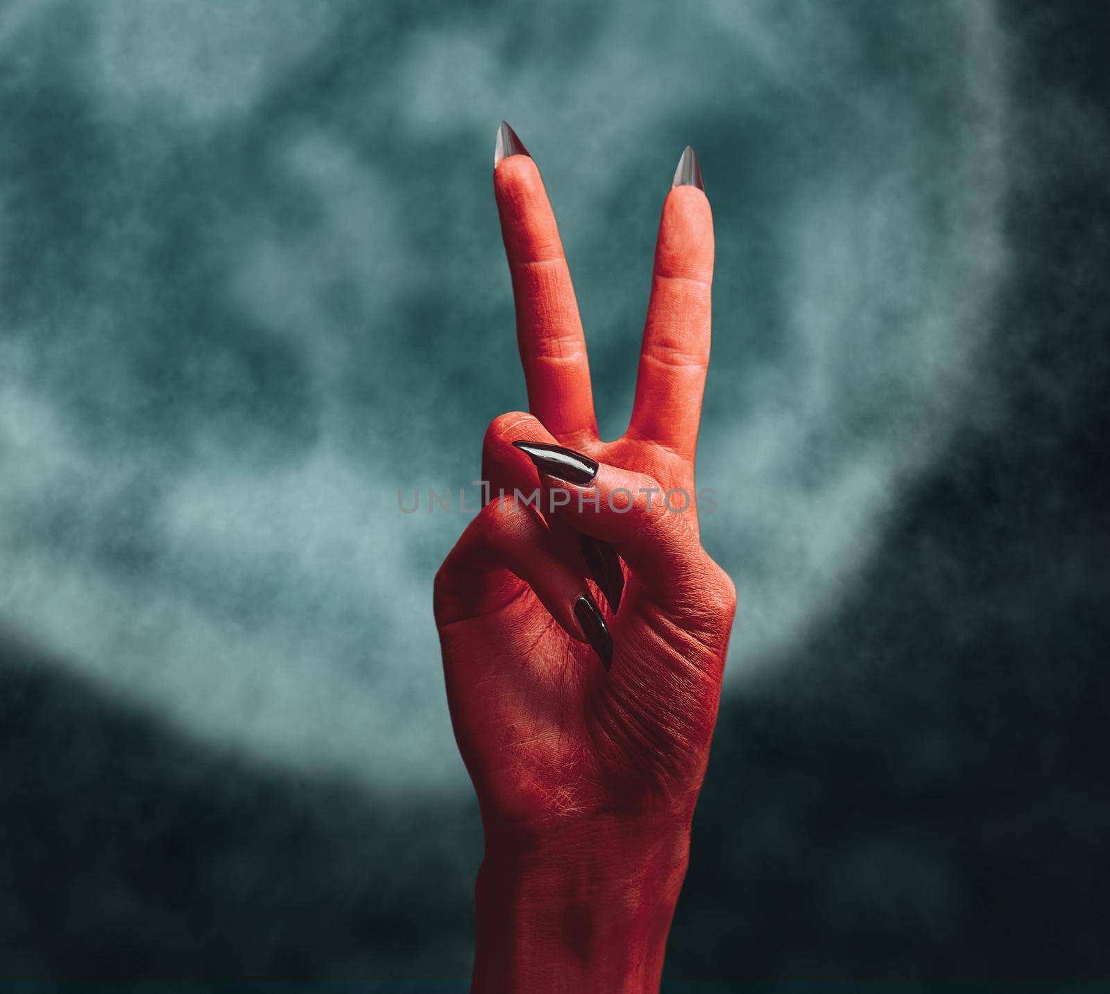 Red devil hand on dark background, peace hand sign. Halloween or horror theme