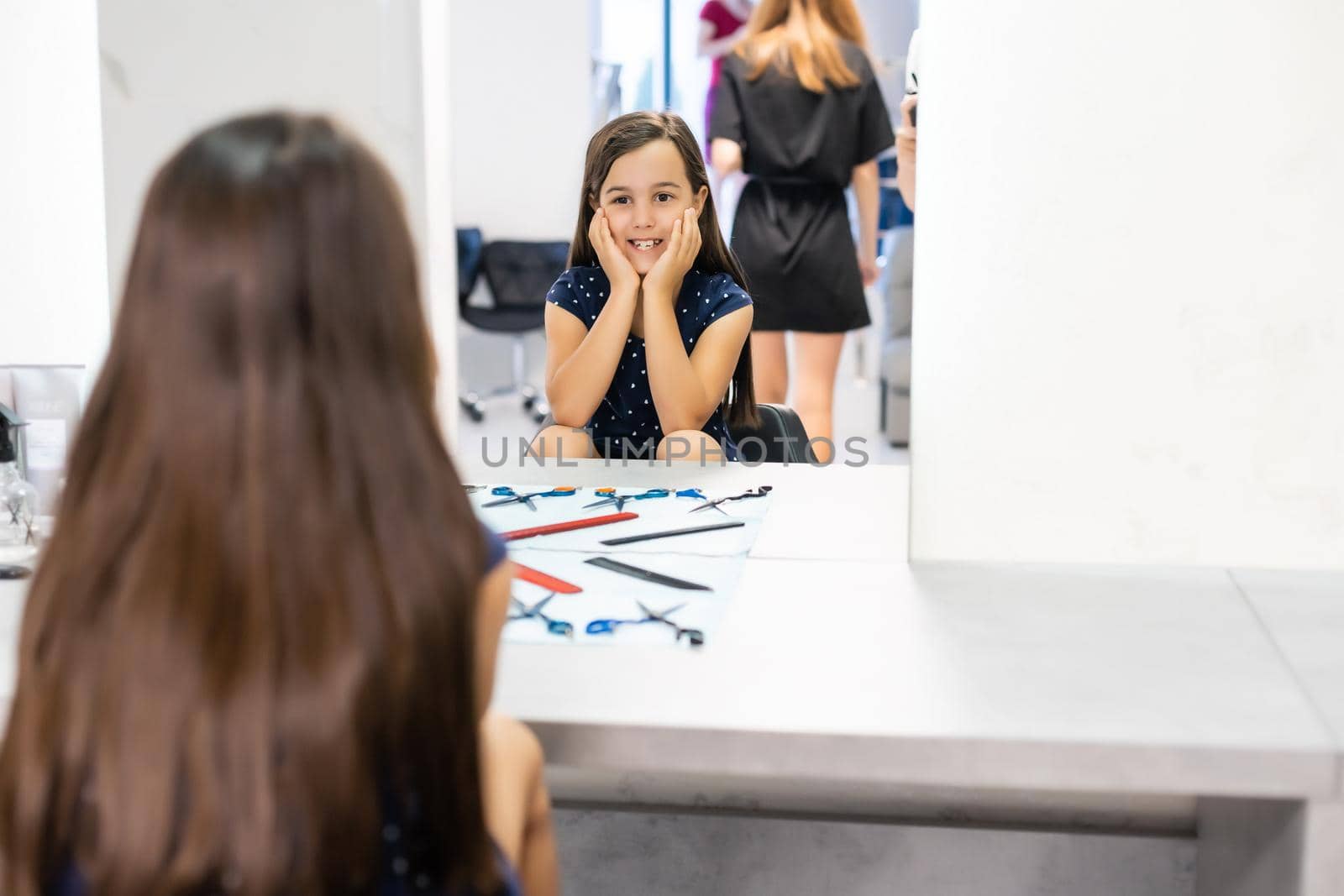 Portrait of pretty little girl seating at table with accessories in a hairdressing salon