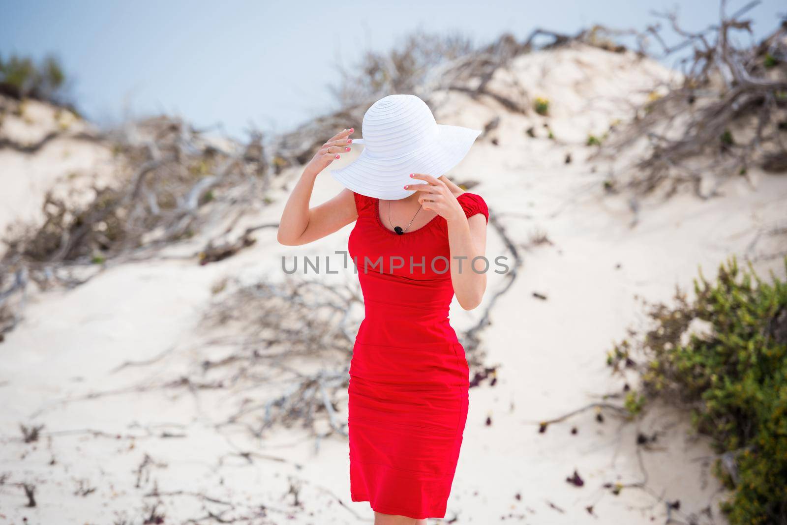 beautiful young woman in evening red dress and white hat on a background of a sand desert