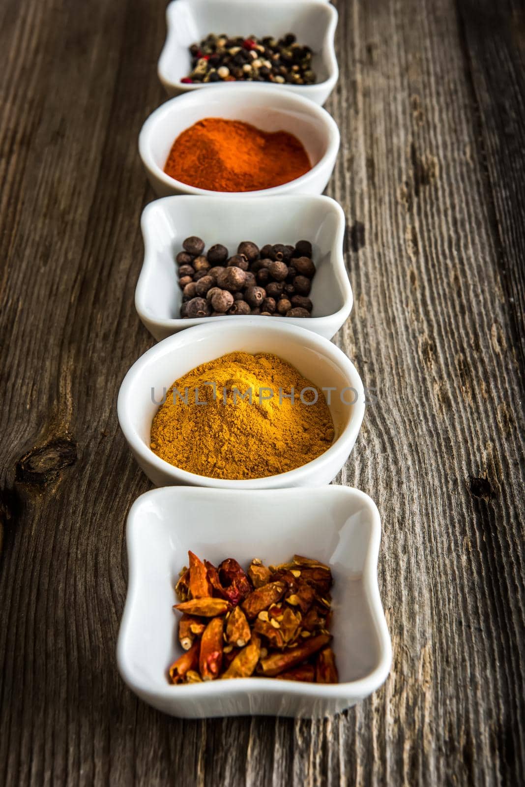 different spices in white bowls in a row on wooden background