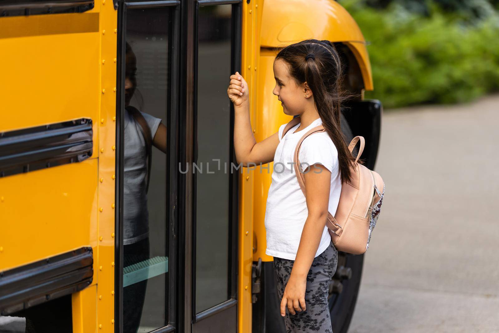 Girl with backpack near yellow school bus. Transport for students by Andelov13