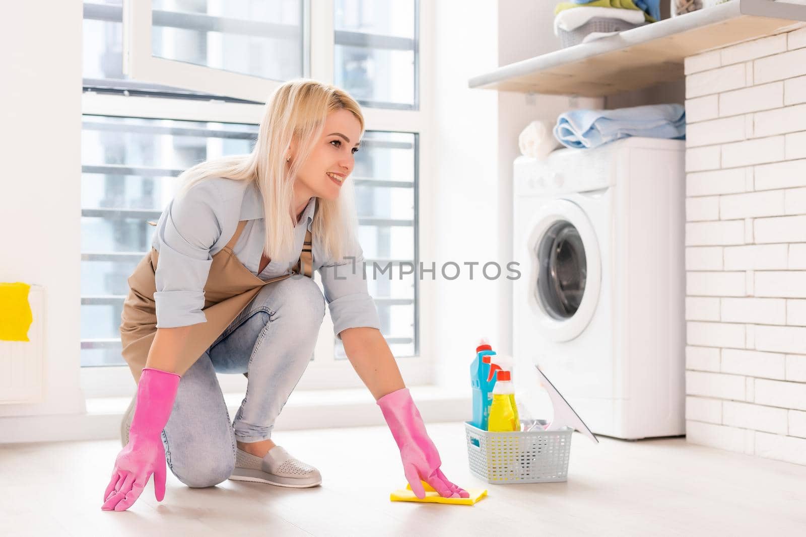Young woman holding cleaning tools and products in bucket in apartment
