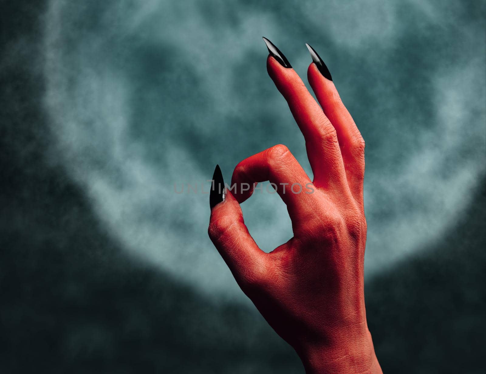 Red demon or devil hand with gesture OK on background of full moon. Halloween/horror theme