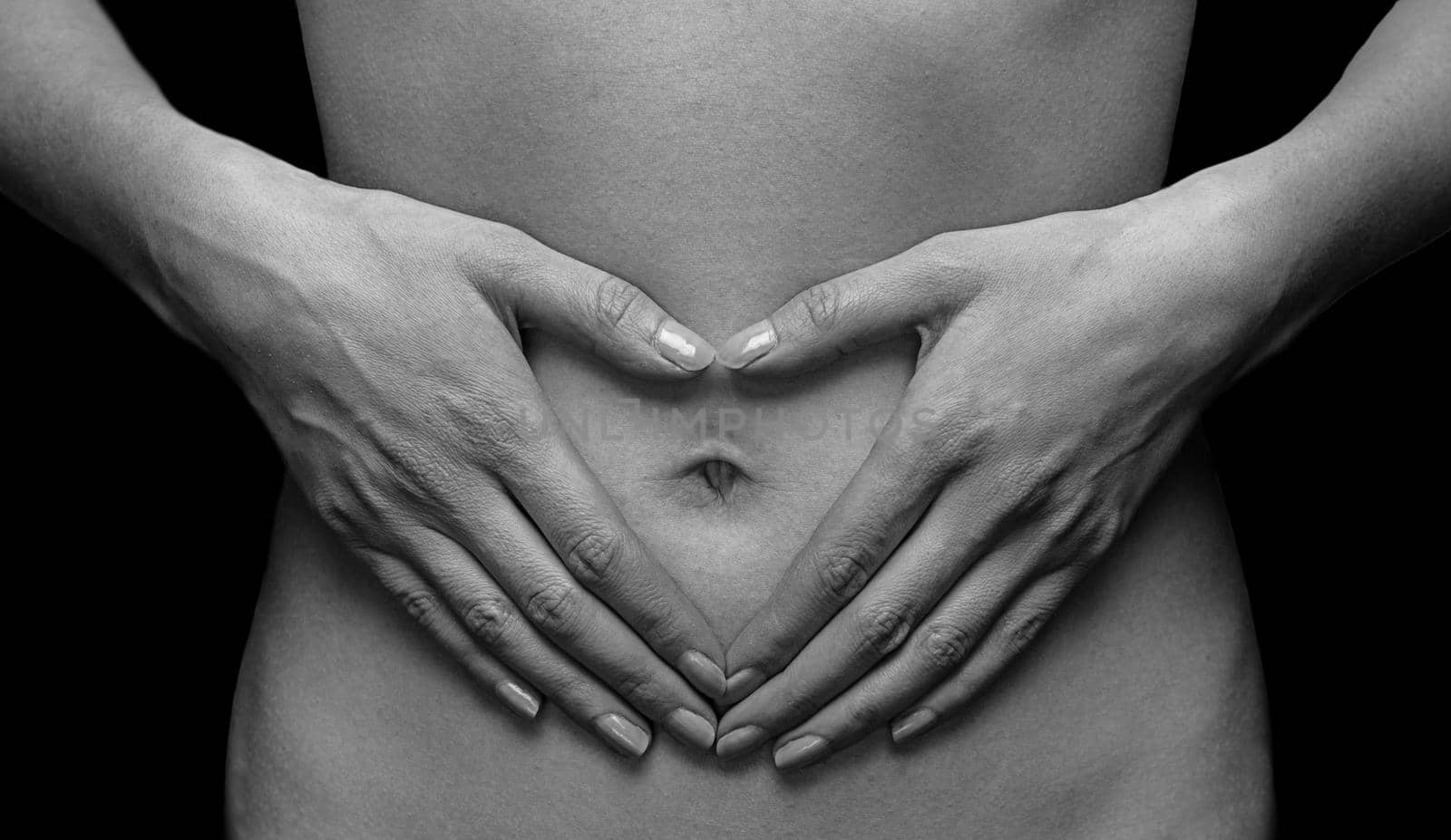 Unrecognizable woman holds her hands in heart shape in front of her abdomen, monochrome image