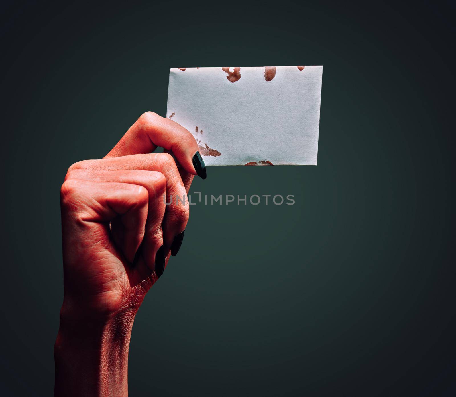 Red demon or devil hand holding empty card on dark background, space for text. Halloween/horror theme