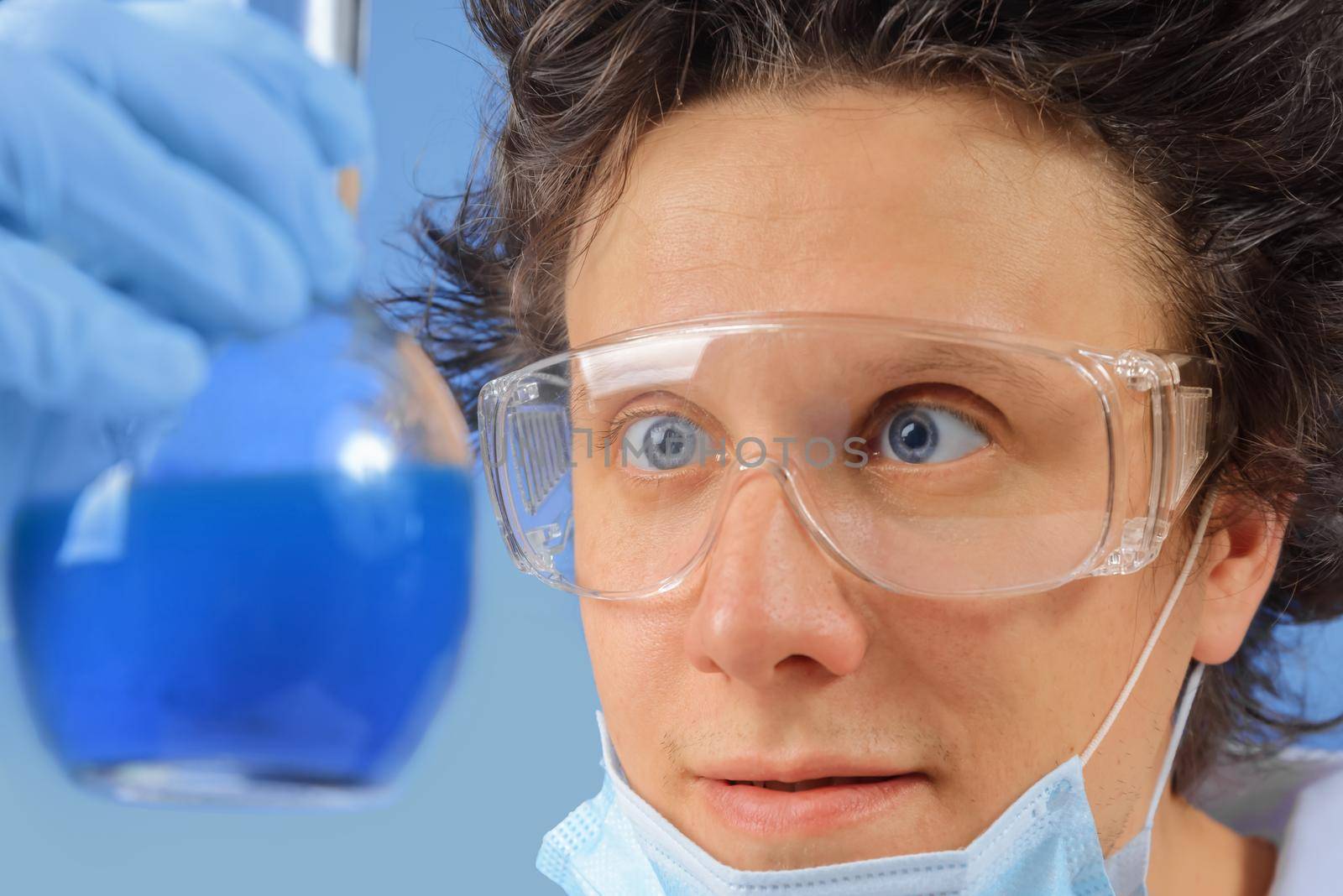 Happy scientist examines laboratory flask with blue liquid