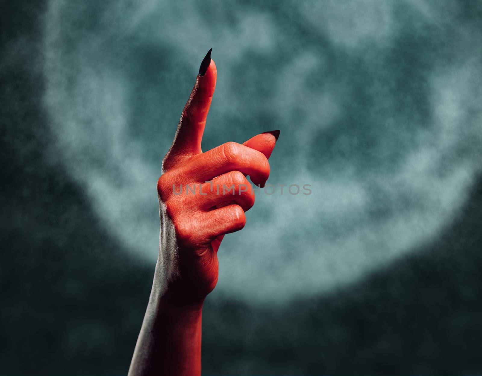 Red demon hand with gesture pointing upward on background of full moon, space for text. Halloween or horror theme