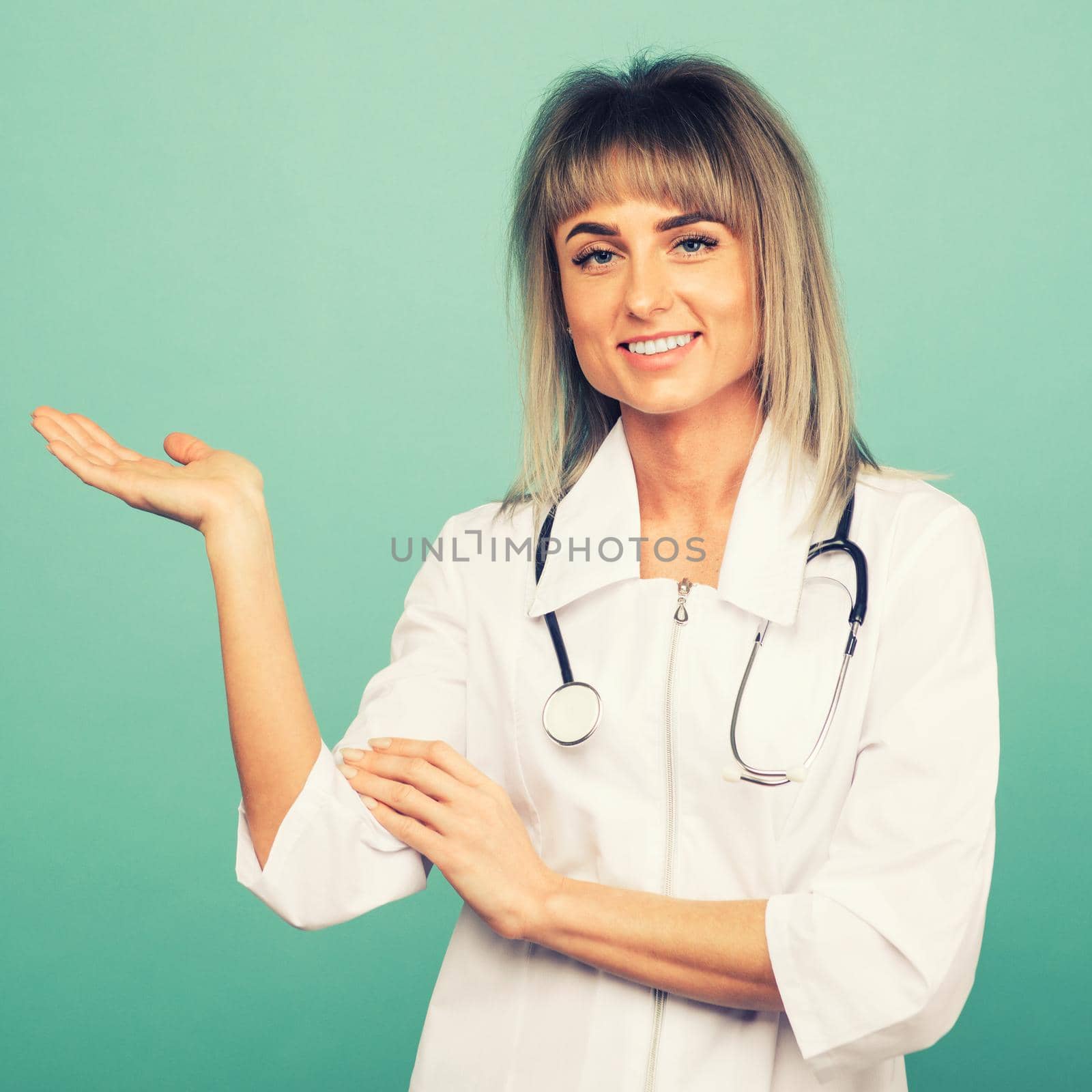 Smiling young female doctor with a stethoscope shows something on the palm on a blue background