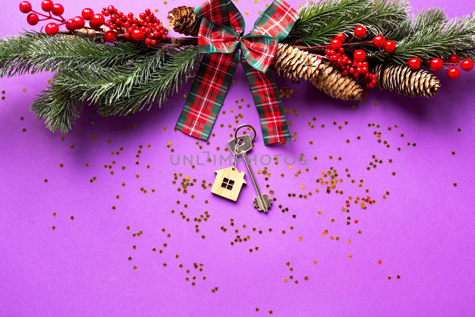 House key with keychain cottage on a festive background with Christmas tree, lights of garlands. Happy New Year-purple background, gift, greeting card. Purchase, construction, relocation, mortgage by Simol