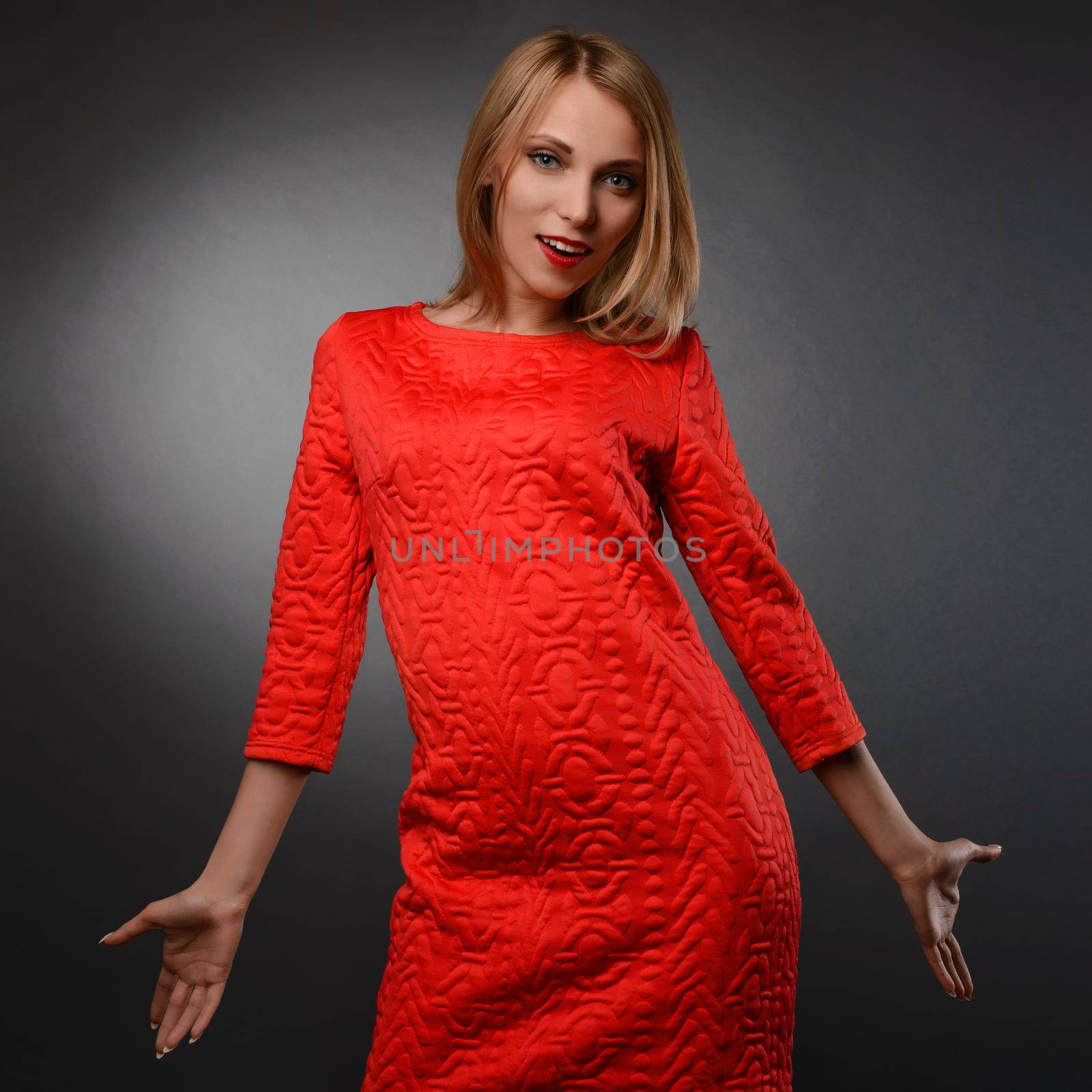 Girl in a red dress is standing with her arms outstretched. Female model. Surprised woman in studio