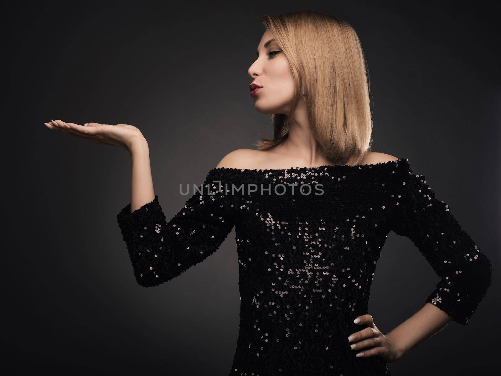 Attractive blond woman blowing kiss against grey background. Curvy young female model in dress.