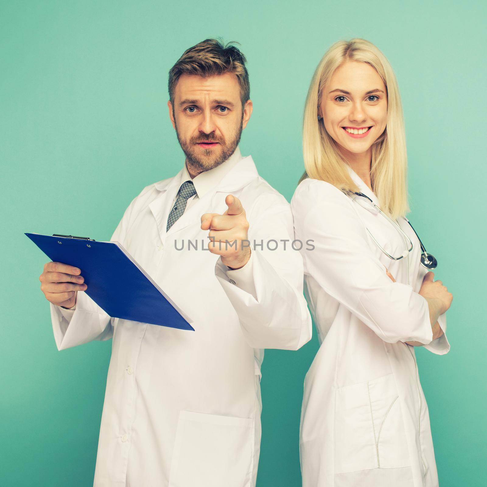 Happy medical team of doctors, man pointing to camera and smiling woman, isolated over blue background. toned