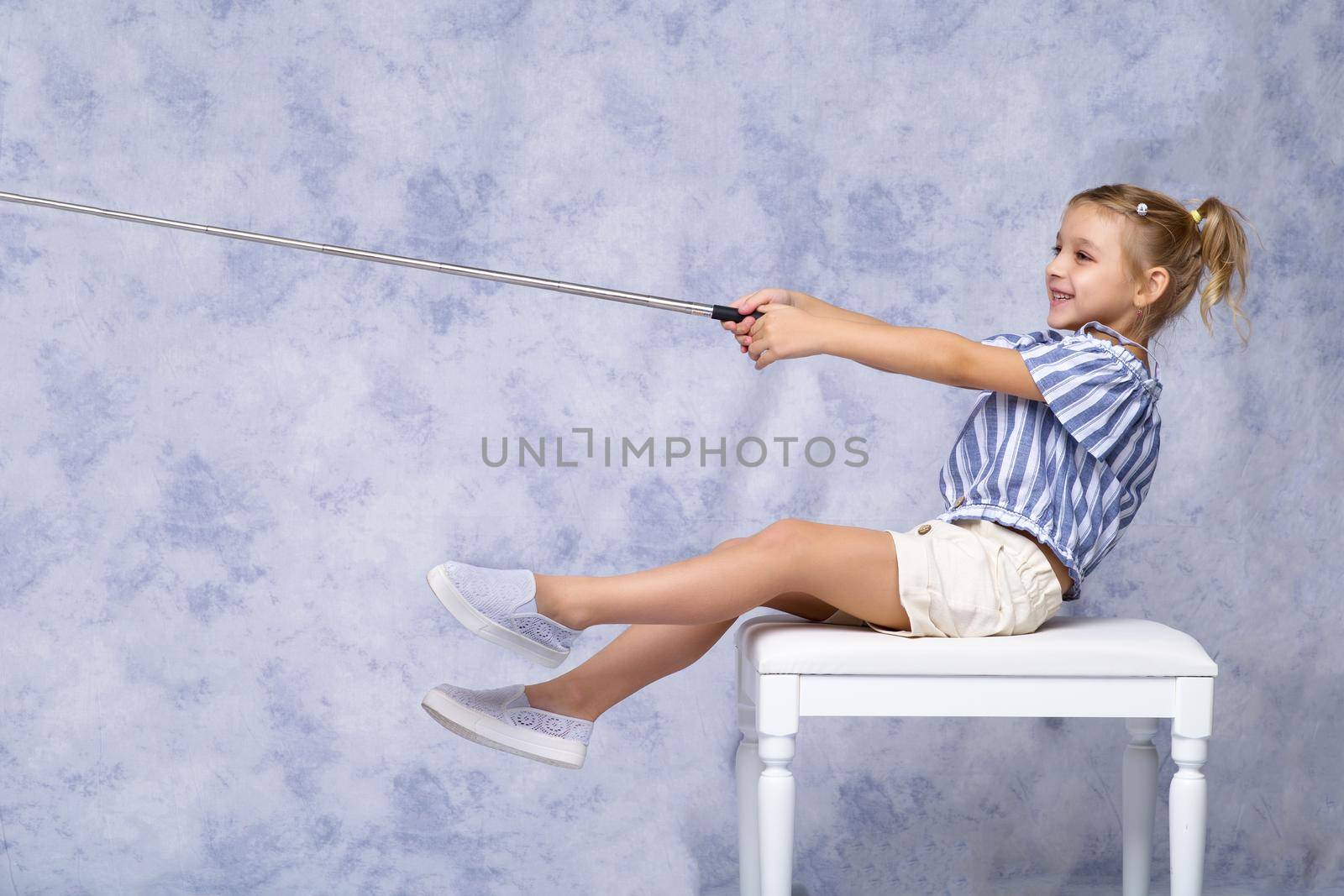 A cute little girl attracts attention by pointing at something with her stick. Simulates fishing with a rod. The concept of advertising goods and services. Isolated on white