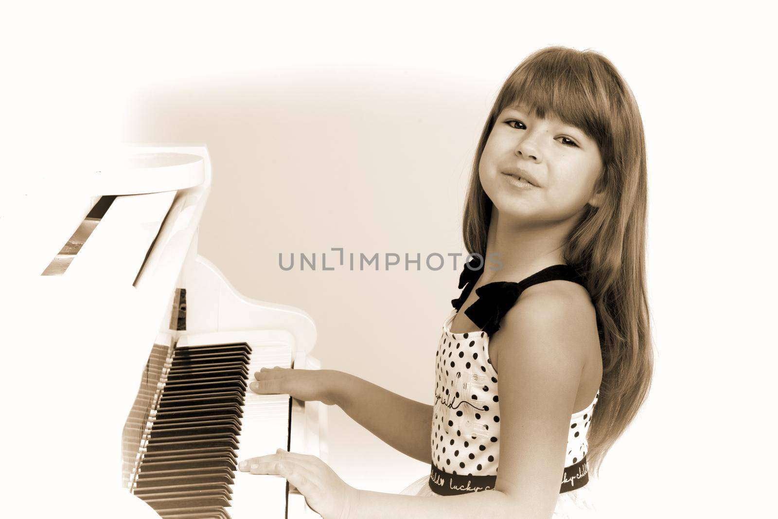 Lovely girl posing at white grand piano Vintage looking photo of beautiful child playing piano at music lesson. Portrait of adorable preteen long haired girl in nice dress posing at camera