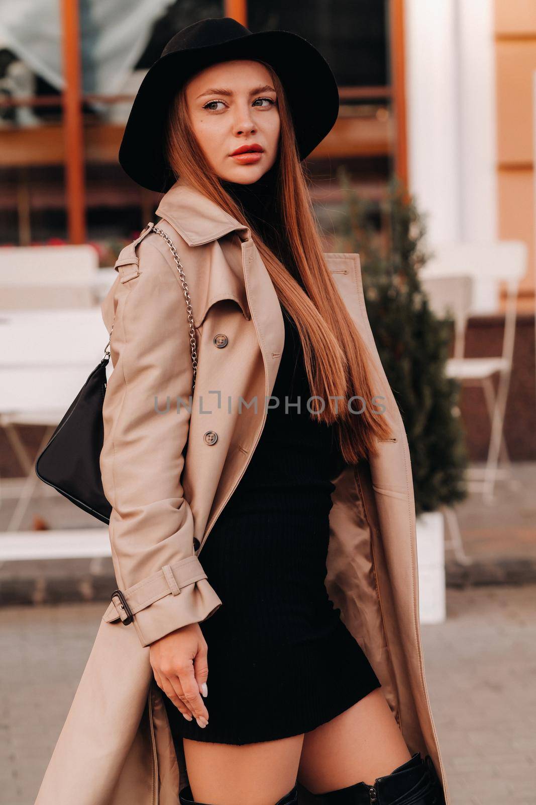 Stylish young woman in a beige coat in a black hat on a city street. Women's street fashion. Autumn clothing.Urban style.