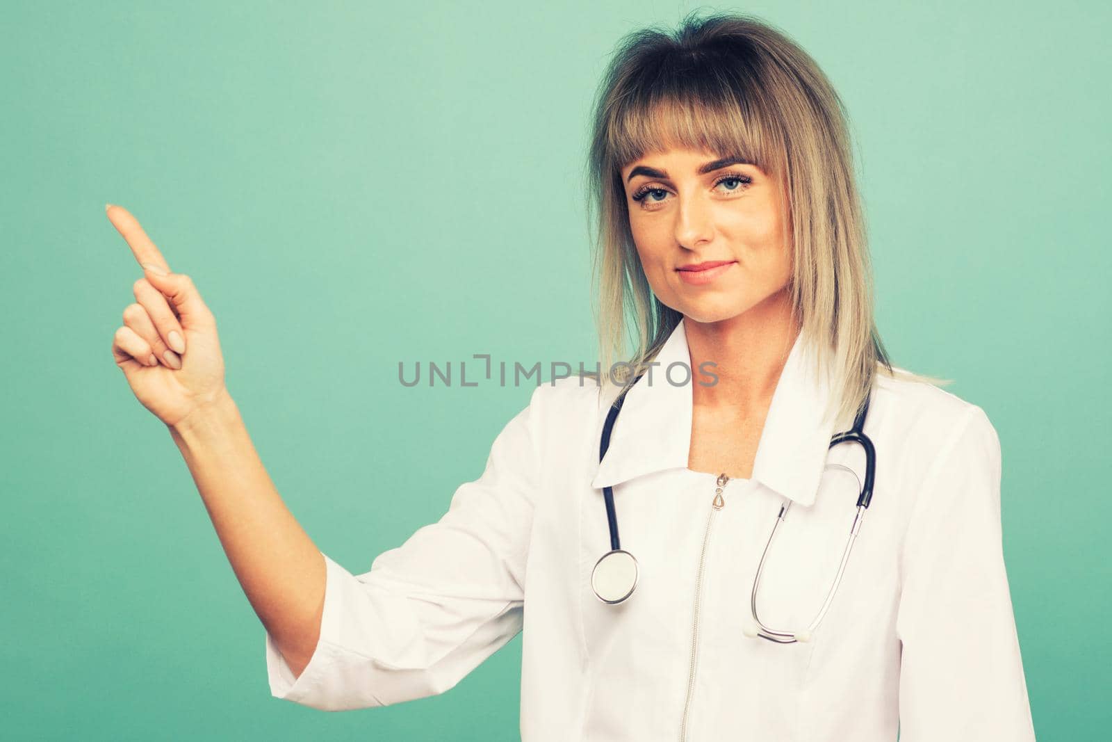 Smiling young female doctor with a stethoscope points up her fingers on a blue background