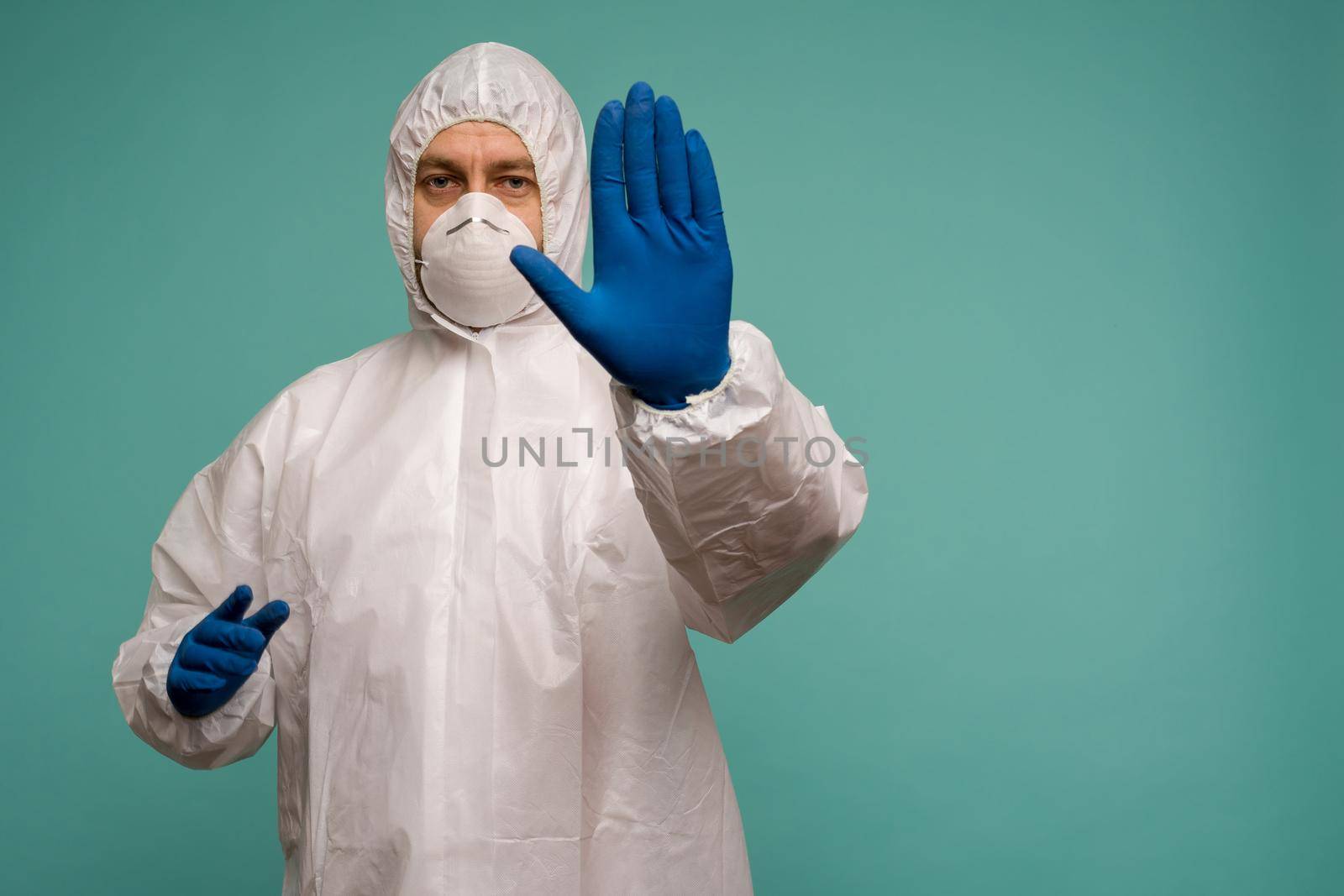 A male doctor in protective overalls and a mask shows stop sign. Coronovirus protection concept in China. - image