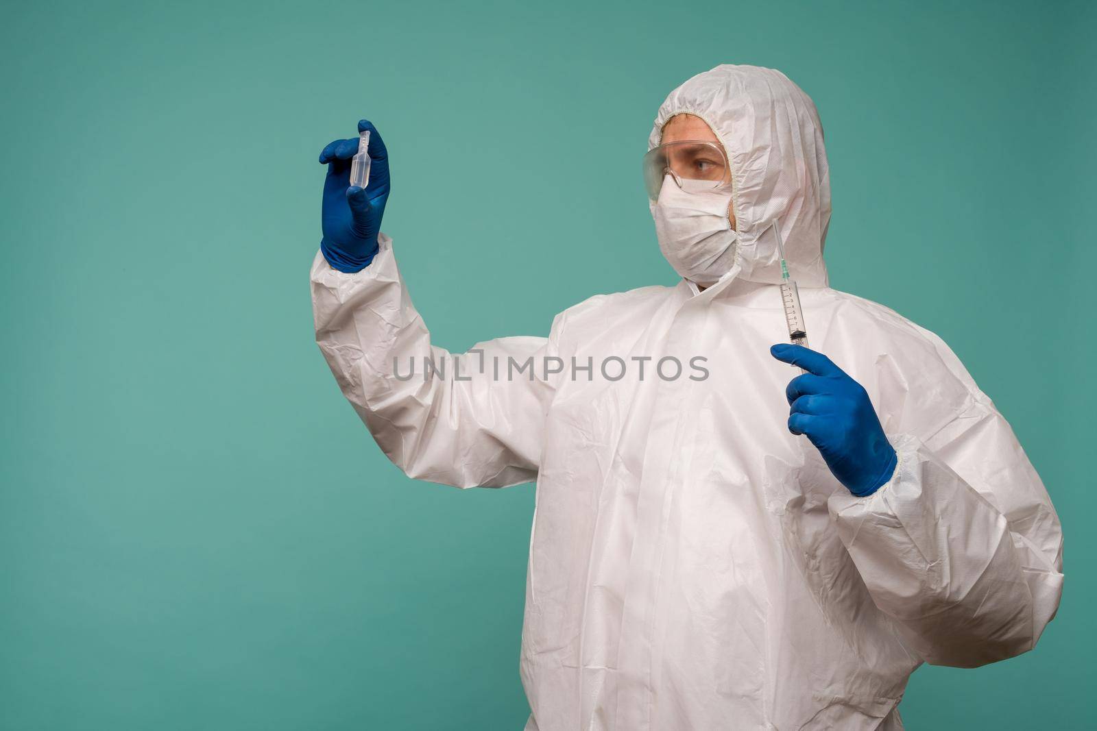 A male doctor in protective overalls and a mask holds an ampoule with a vaccine and syringe in his hands. Coronovirus protection concept in China. - image