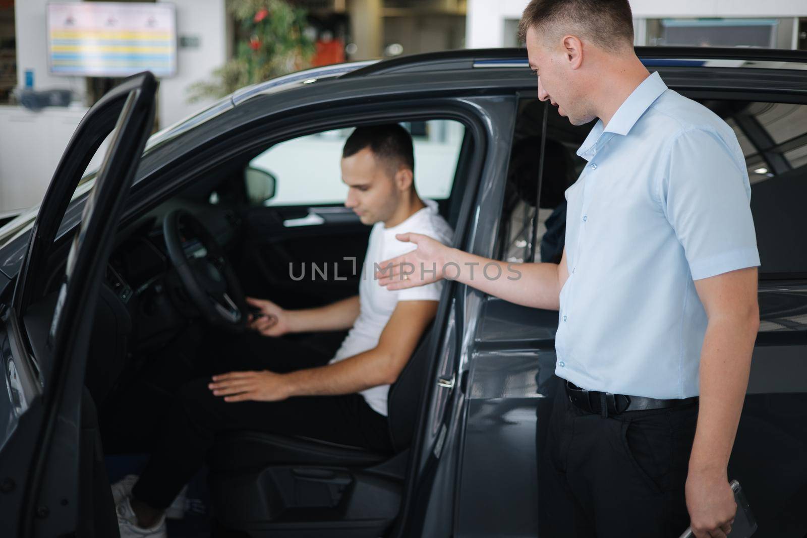 Salesperson selling cars at car dealership. Man choosing car in car showroom.