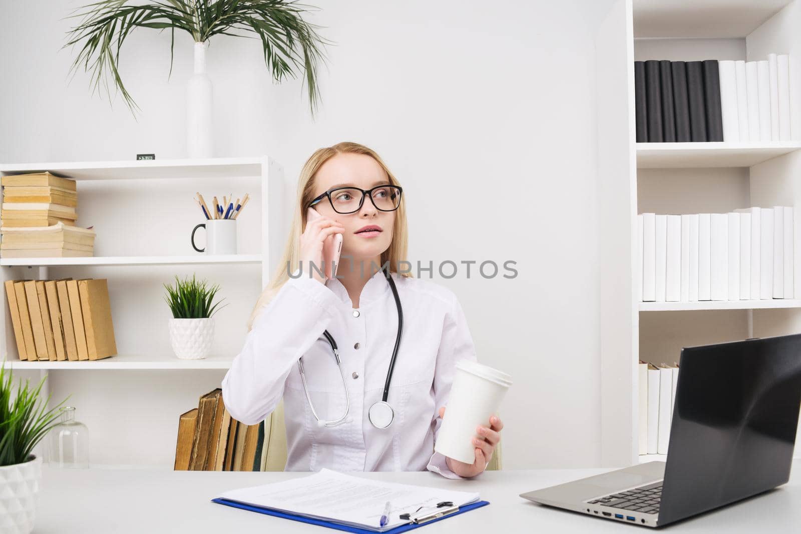 Portrait of a beautiful smiling woman doctor while talking on the smartphone and complete a medical information - Image