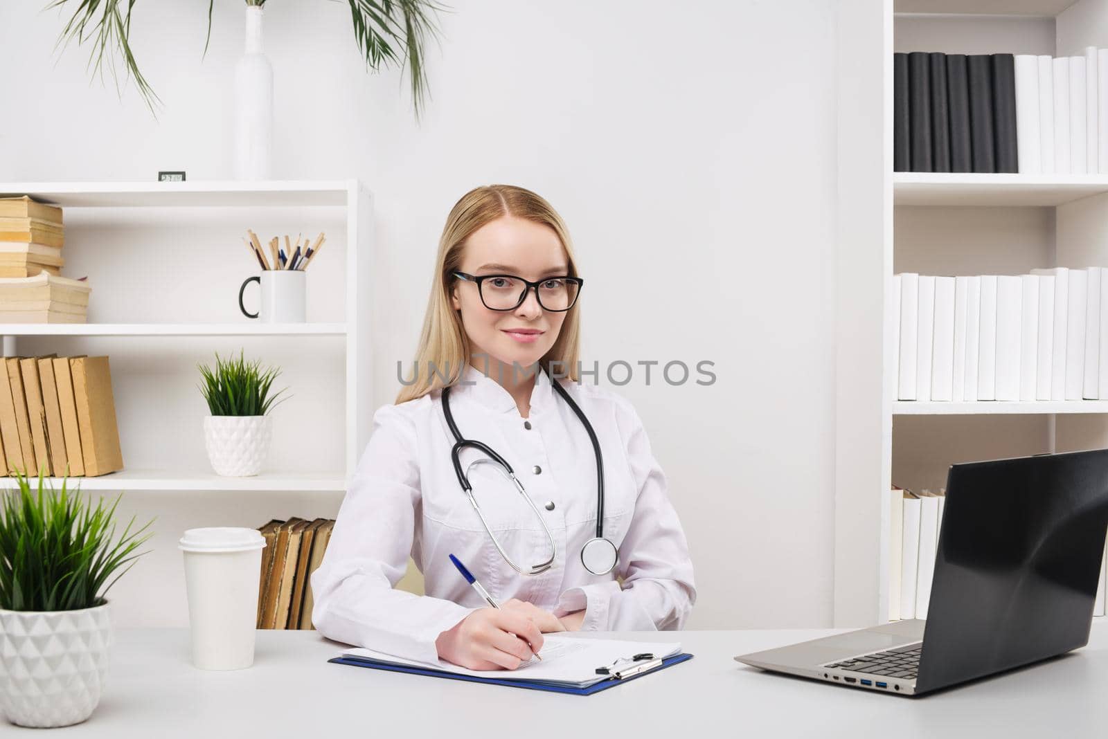 Young beautiful doctor woman working happy and smile in hospital, sitting on table, medical concept