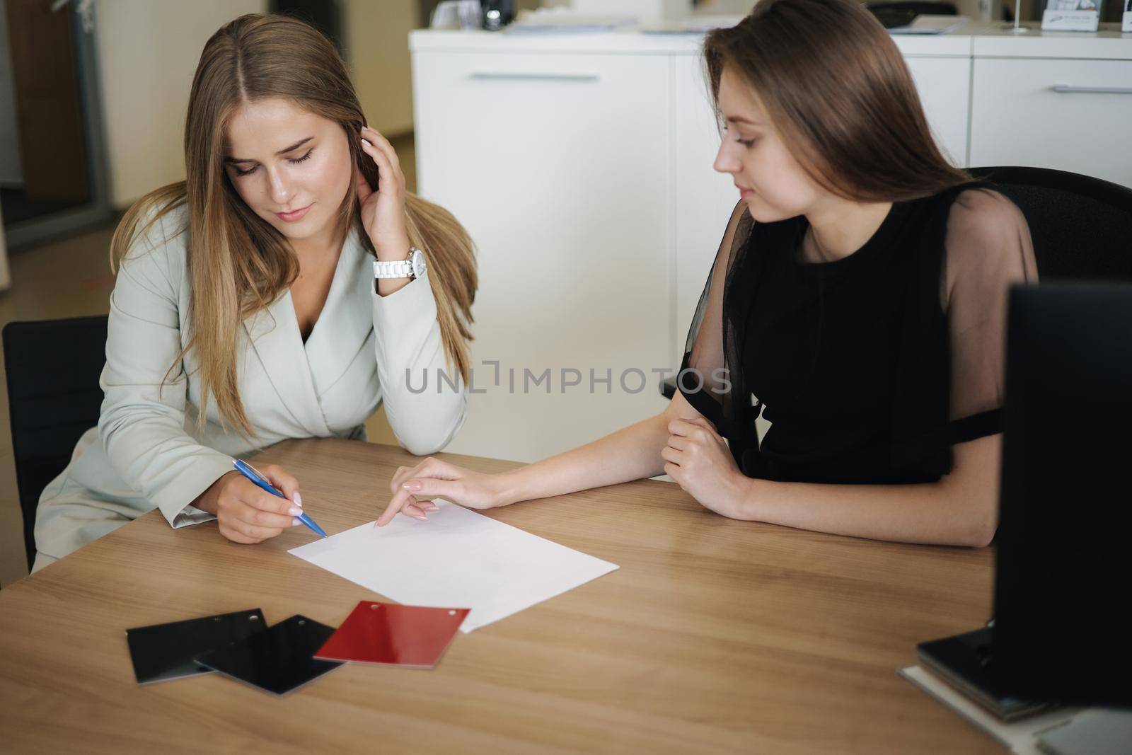 Woman choosing and buying car at car showroom. Car salesman helps them to make right decision. Female sign documents by Gritsiv