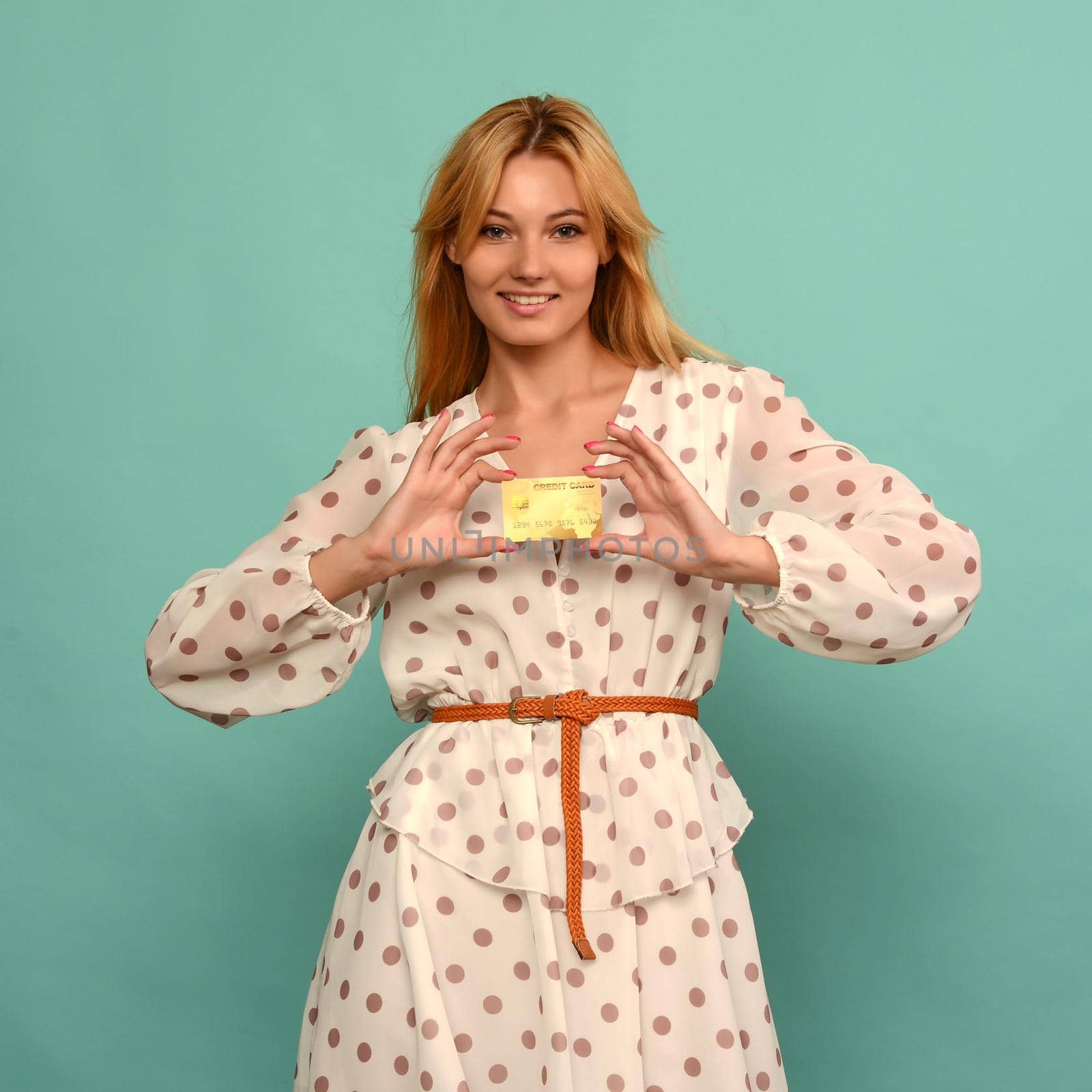 Photo of pleased young woman posing isolated over blue wall background holding debit or credit card.