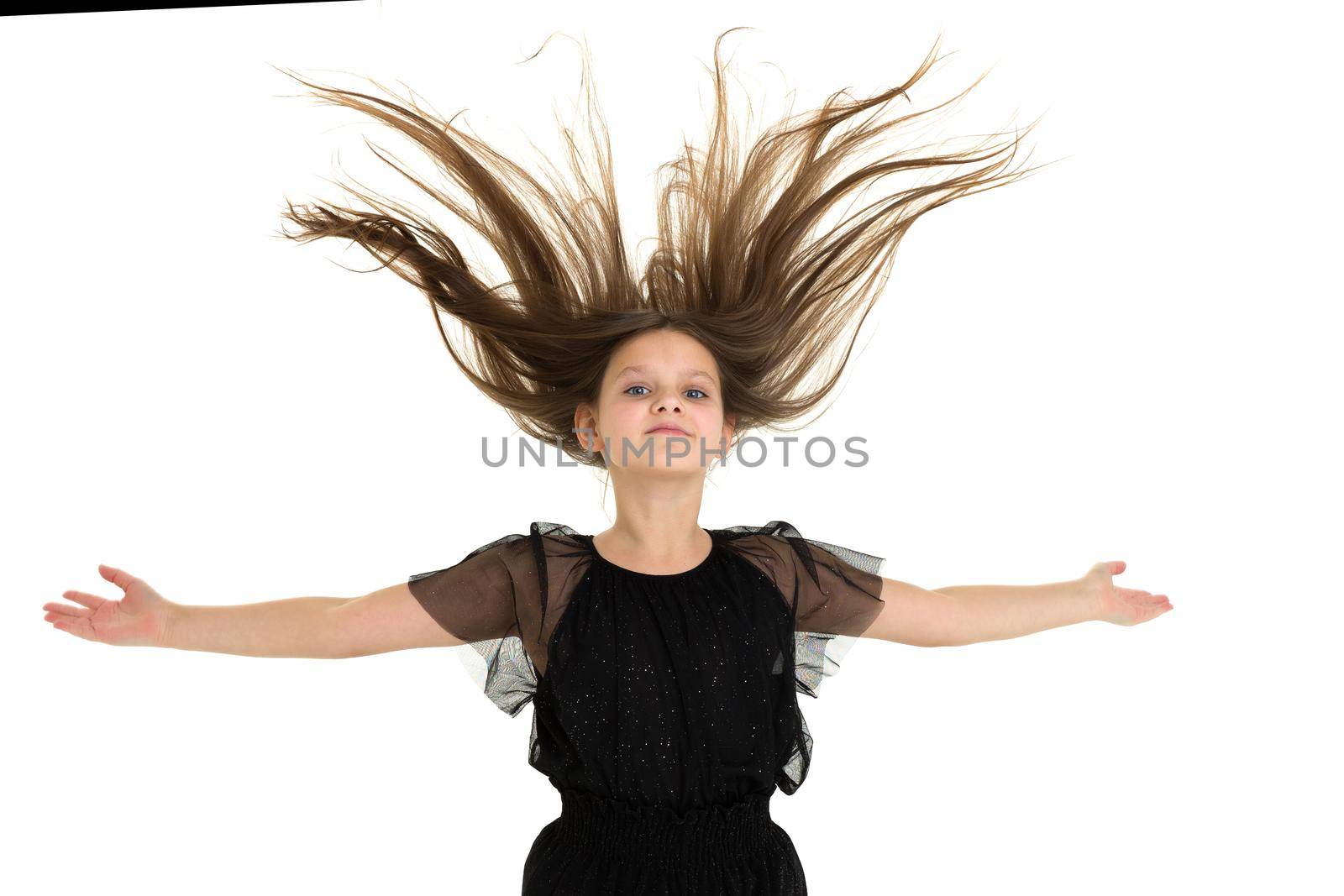 Joyful girl with hair blowing up having fun. Happy cute girl in stylish black jumpsuit jumping with her hands outstretched against white background. Portrait of lovely child with long brown hair