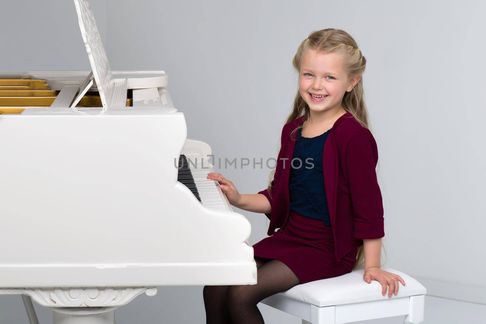 Smiling girl playing the piano. Close-up portrait of adorable long-haired little girl sitting at the white piano. Cute child happily learning to play a musical instrument