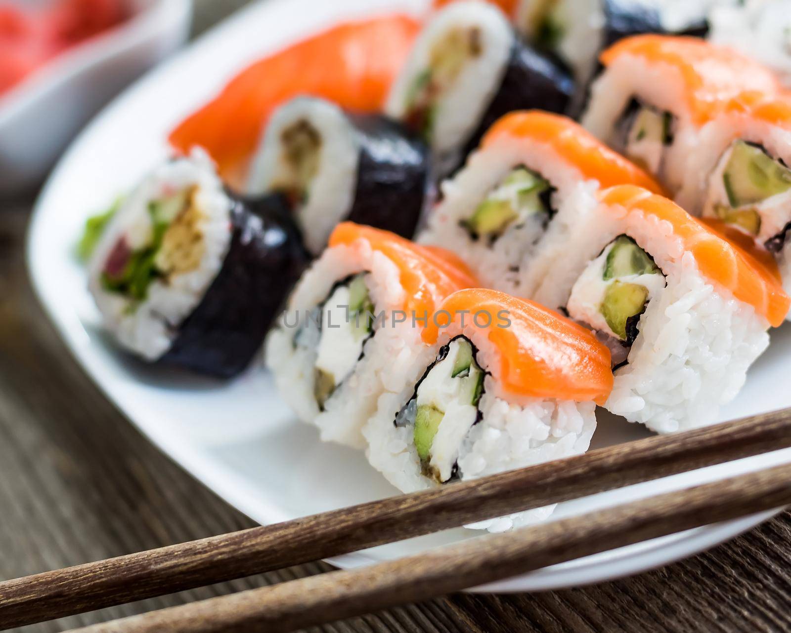 various sushi on white plate with chopsticks on wooden background
