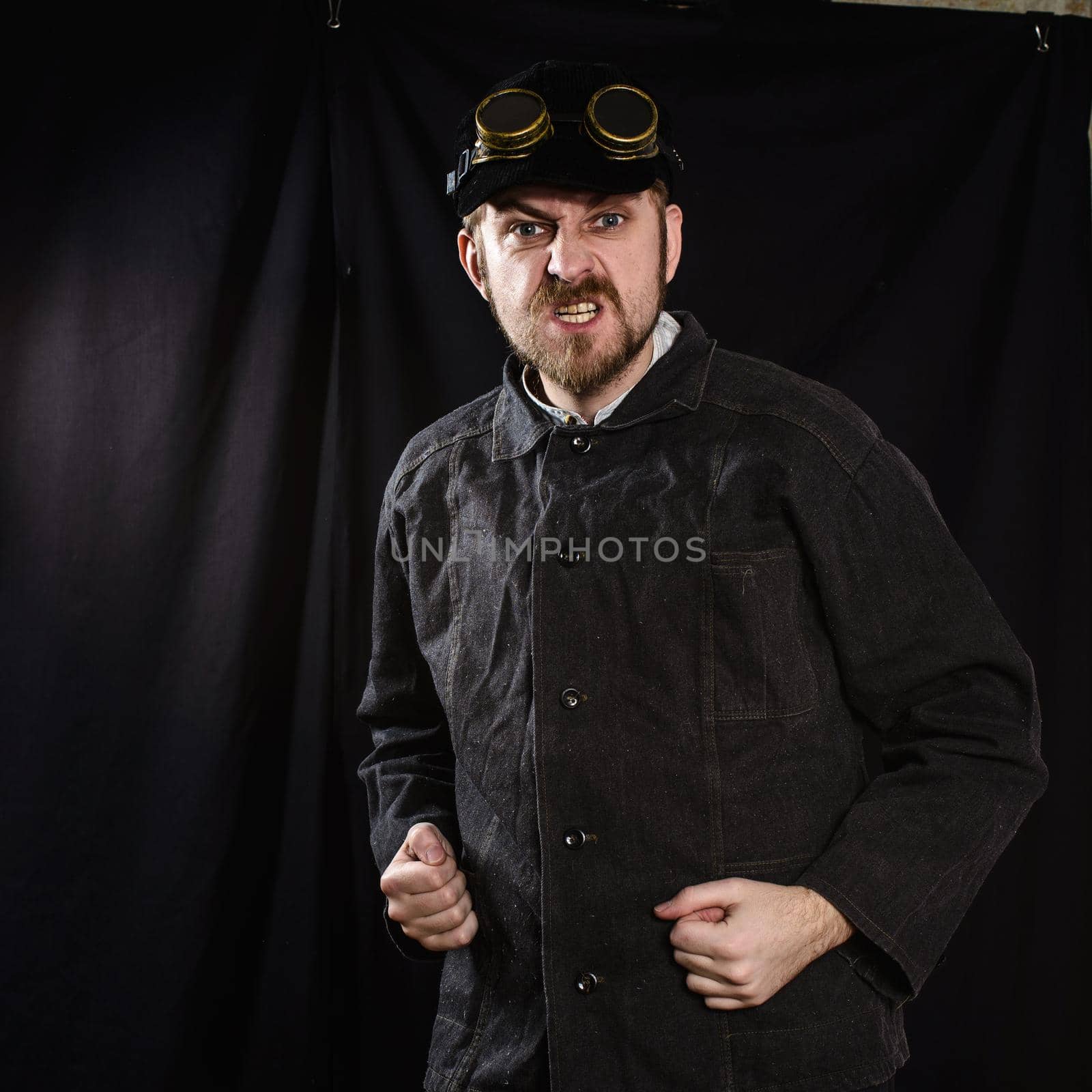 angry black worker in overalls and welding goggles. black background