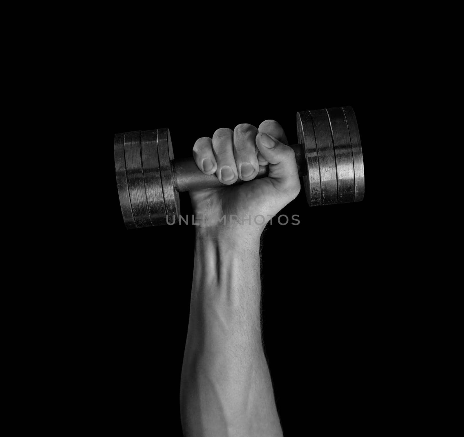 Male hand holds dumbbell on a black background, monochrome image