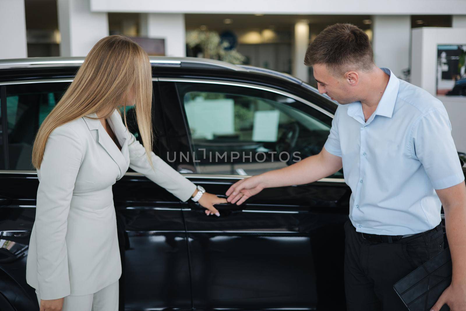 Salesperson shop opporrtunity of each car and help her choos and make right decision. Man and woman in car showroom.