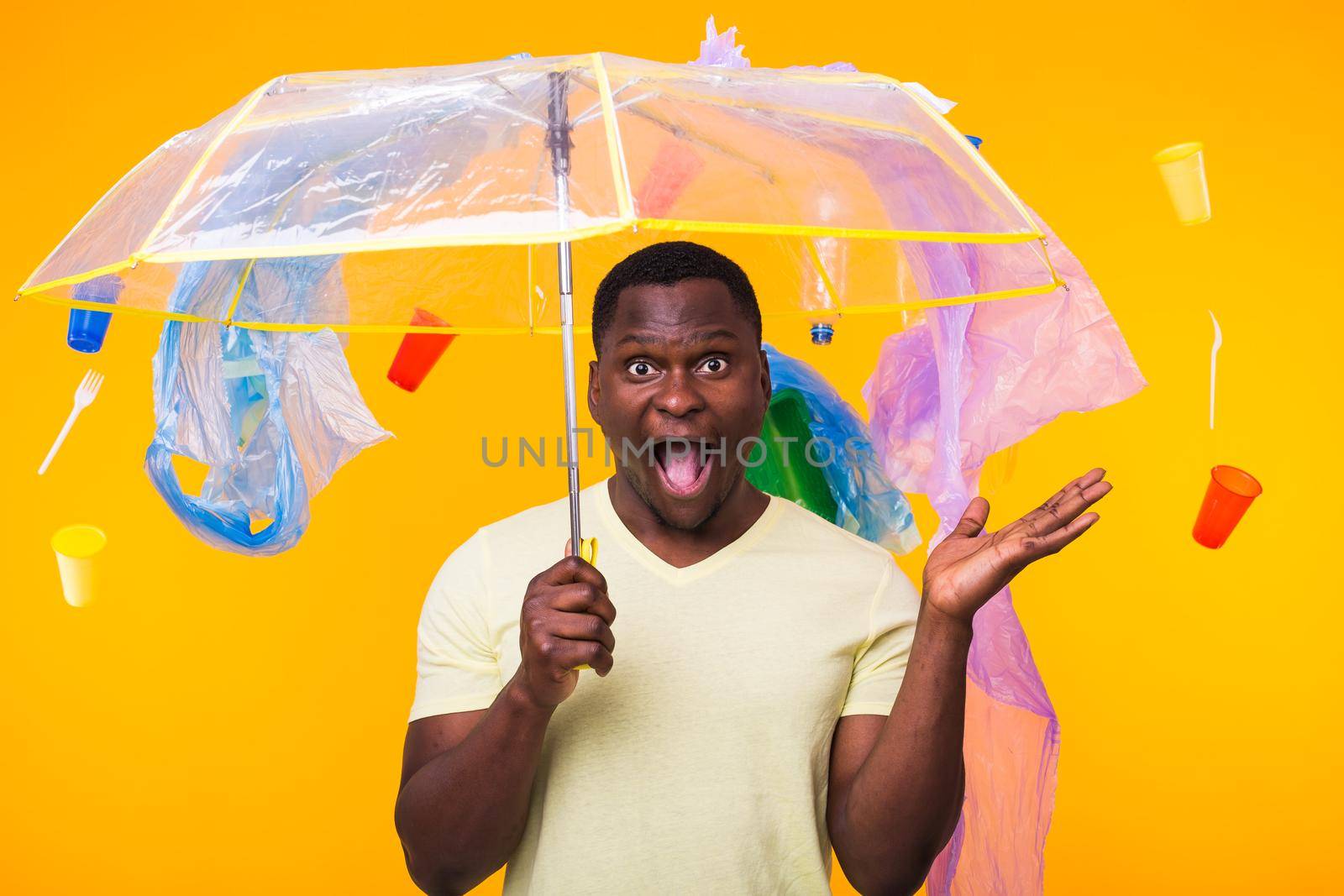 Plastic recycling problem, ecology and environmental disaster concept - Scared man screaming on yellow background with trash. He is worried about ecology disaster.