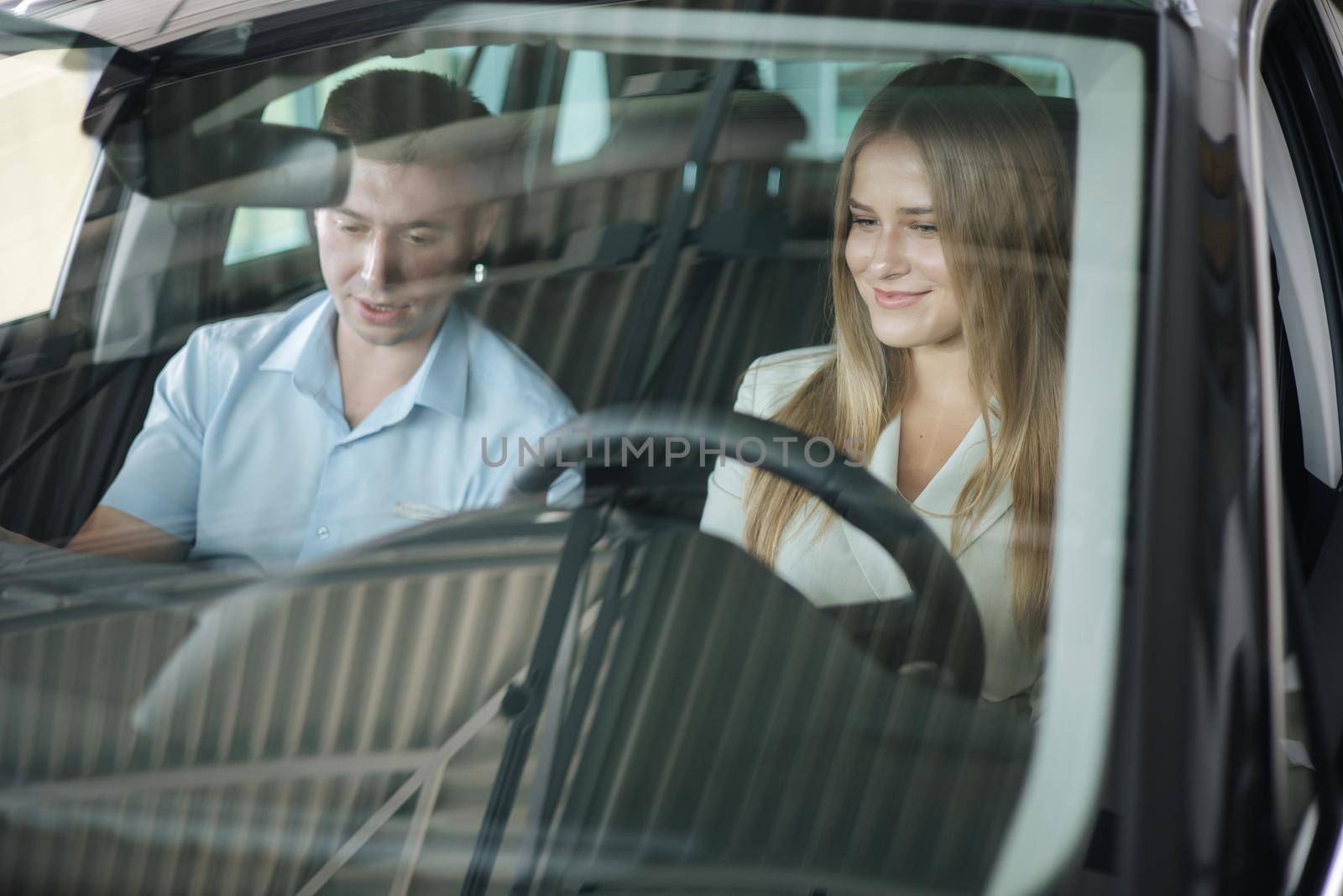 Bussines woman choosing car i car showroom. Salesperson sitting in car with customer and show desing by Gritsiv